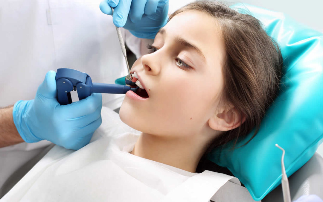 girl in a dentist chair as a dentist works in her mouth