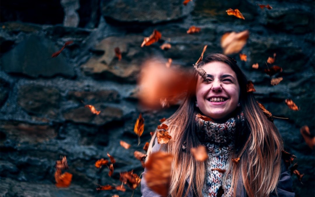 woman smiles as leaves fall around her